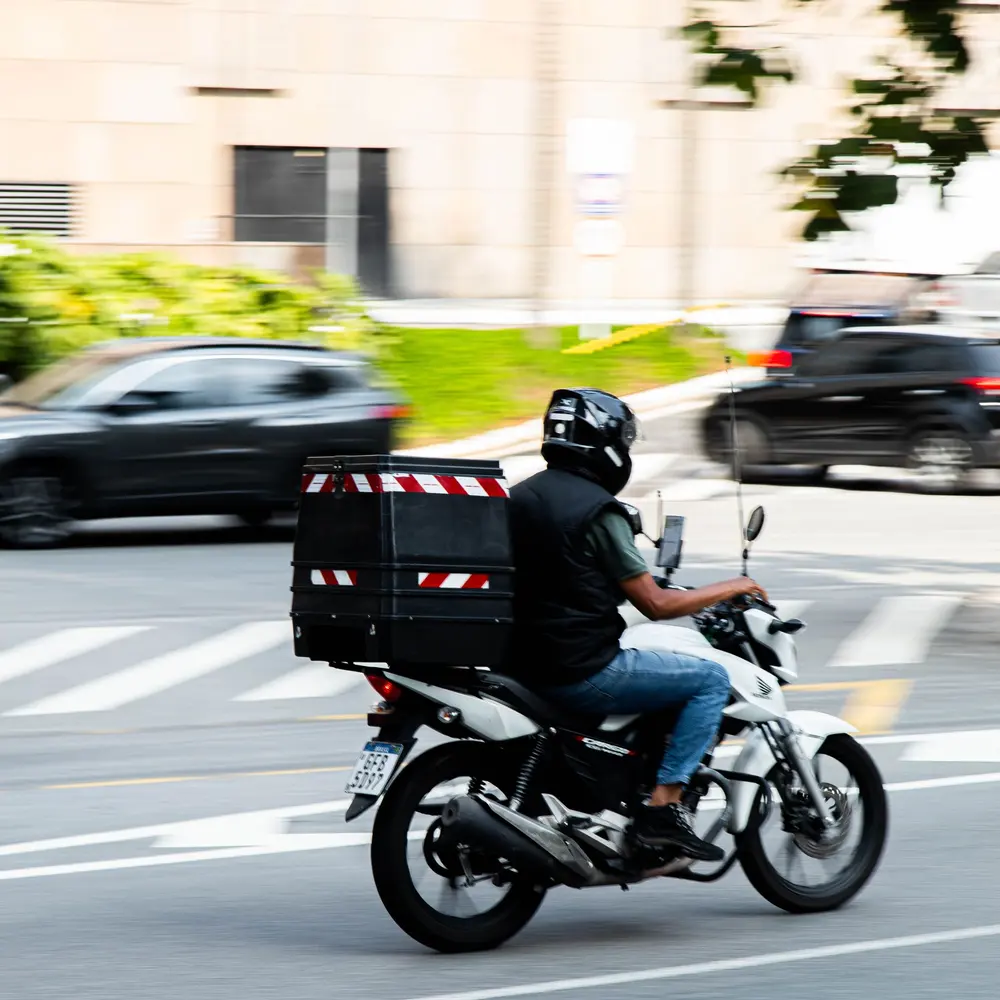 Motoboy com baú pilotando uma moto pela faixa de pedestres na cidade