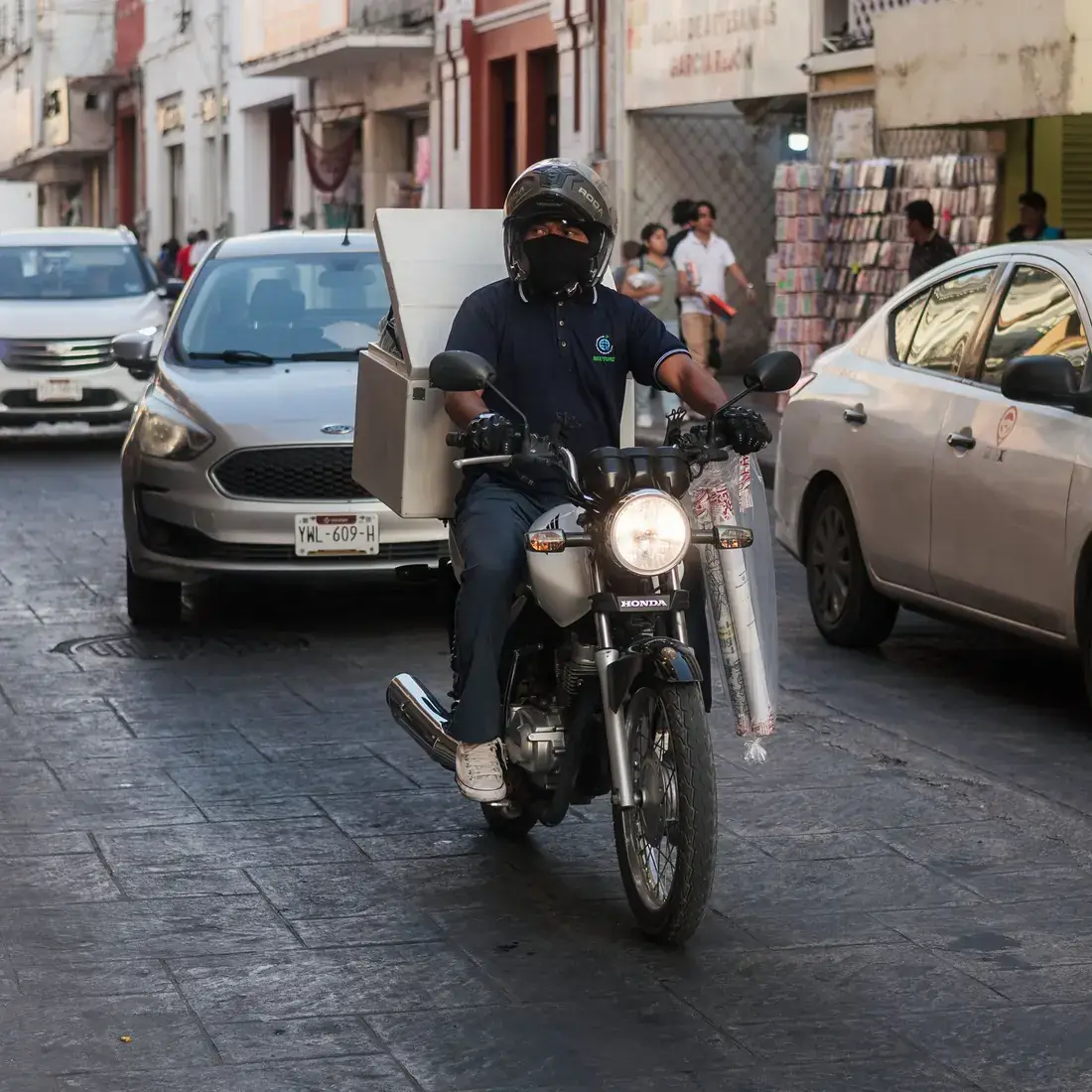 Piloto de moto em rua de paralelepípedo entre carros